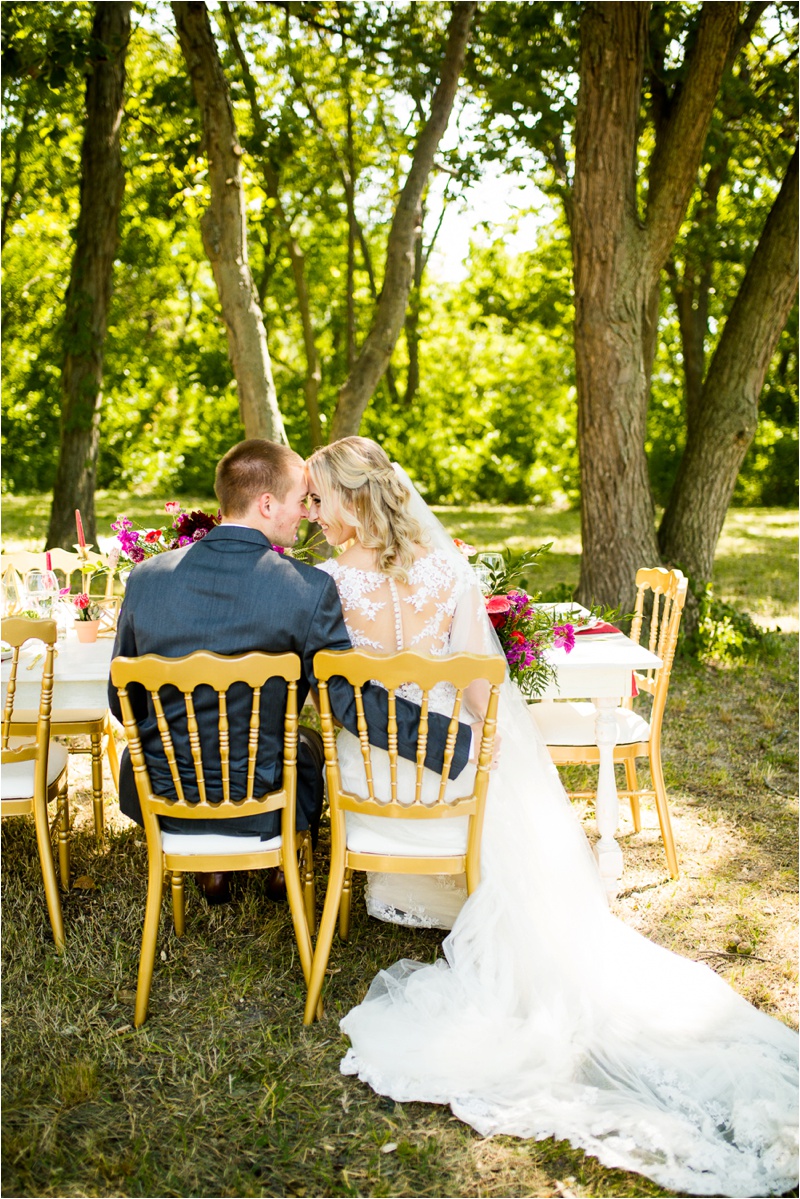 Bride and groom dressed in wedding attire sitting at white farm table