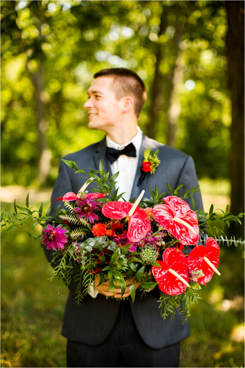 Groom in a dark grey suit with a black tie holding a lush wedding bouquet
