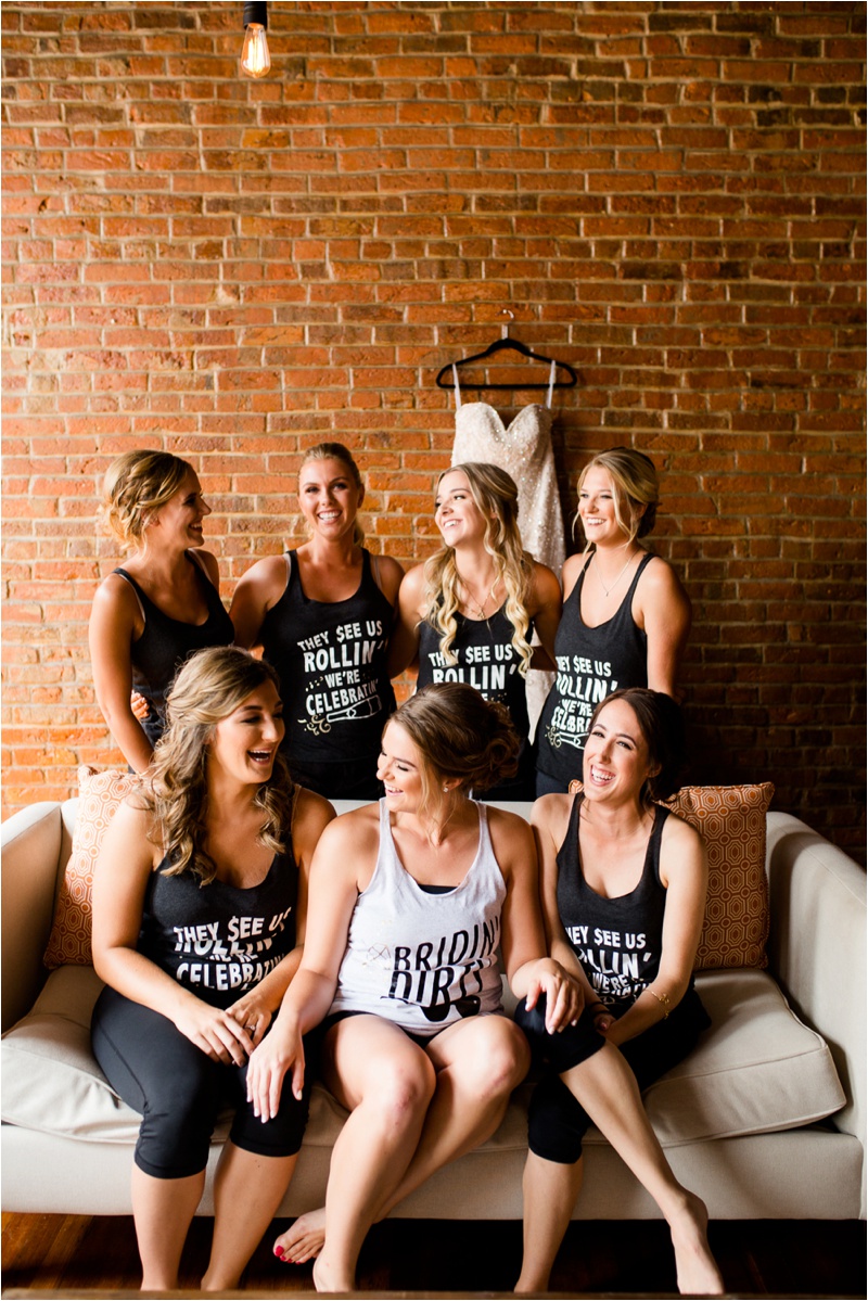 bridesmaids and brides sitting on a small couch with open face brick on the wall behind them
