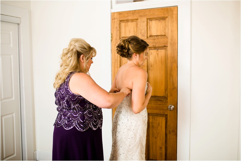 bride holds on to her dress while the mother of the bride laces up her dress