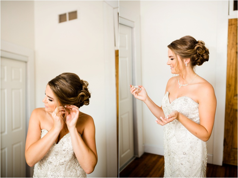 bride standing in her wedding dress puts on earrings and perfume window lit bedroom
