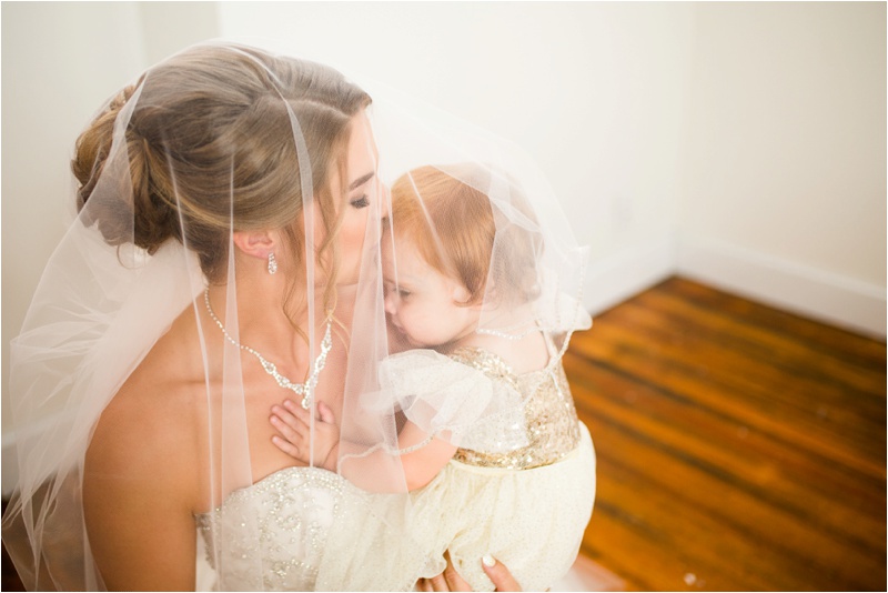 The bride gently kisses her 1 year old daughter as she rests on her shoulder