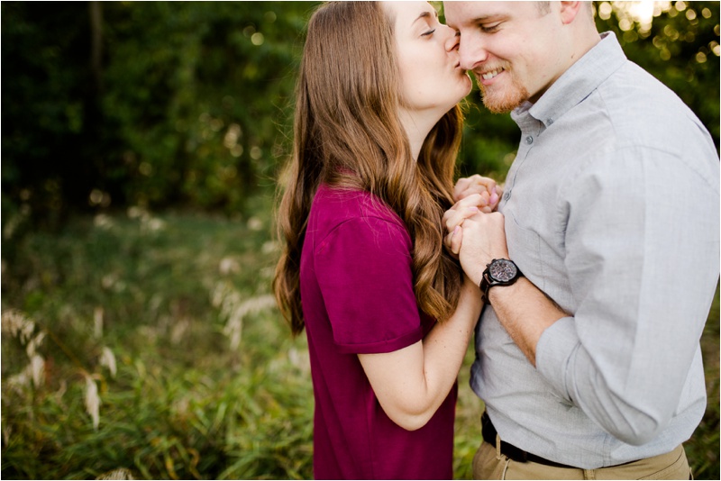 Woman kisses her fiance as he smiles looking down towards the ground