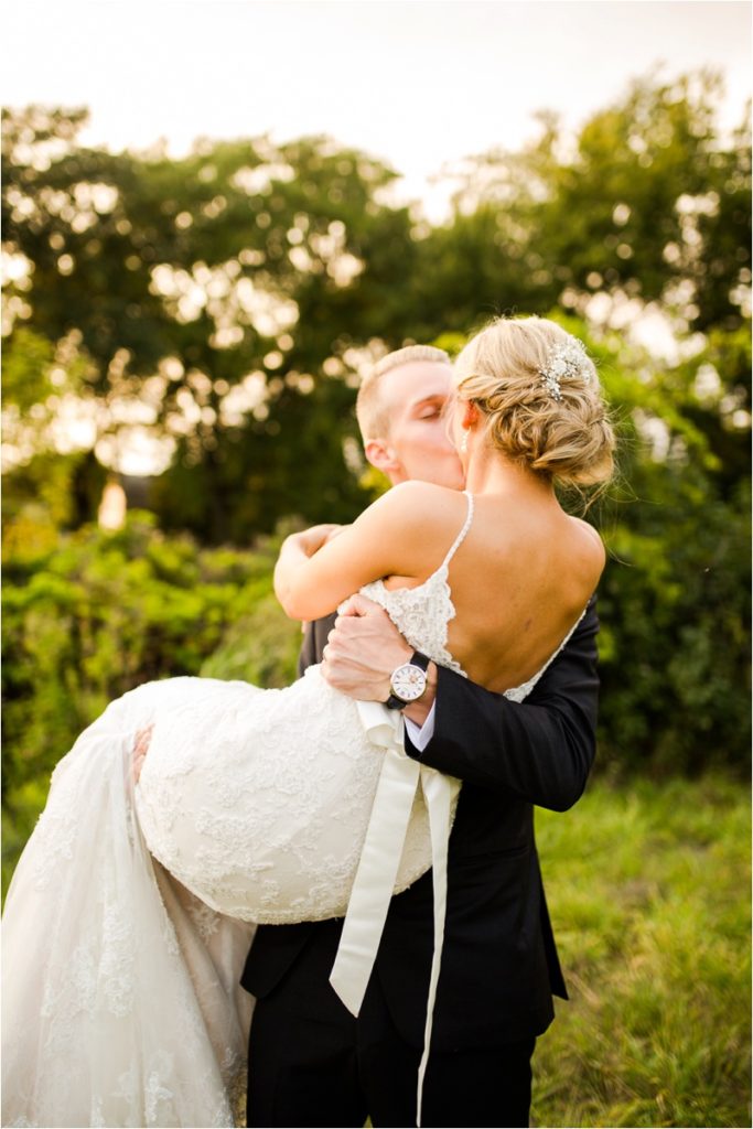 groom in a black suit picks up his bride in her wedding day gown