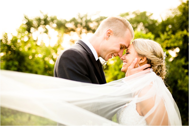 young groom in a suit and young bride in her wedding gown smile as they rub noses together