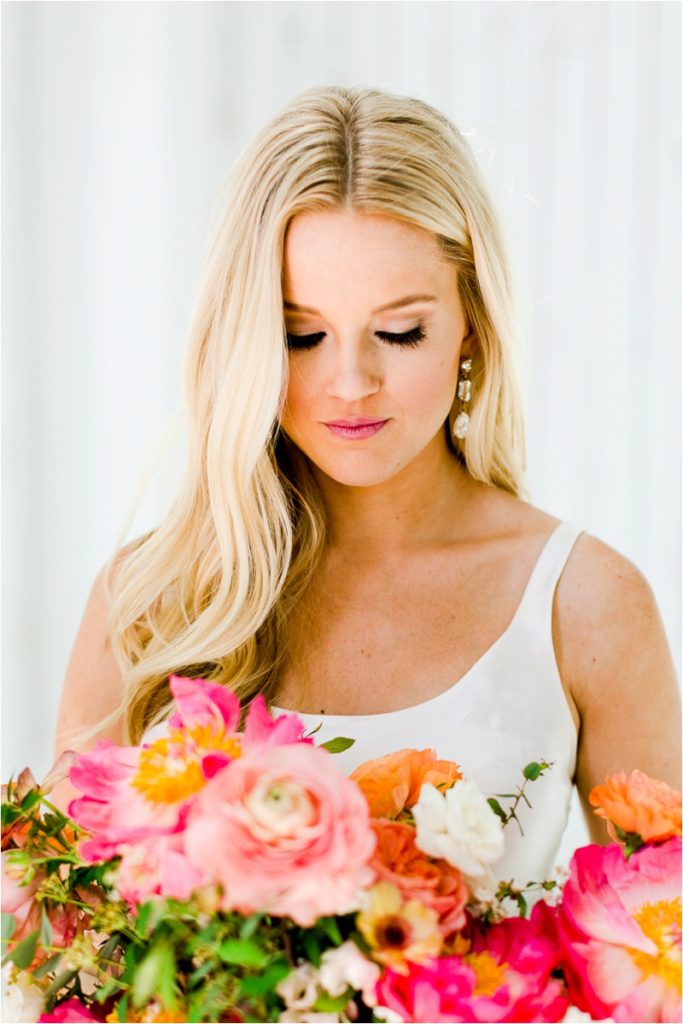 Bridal portrait with soft lighting against white backdrop, bride looking down with natural makeup and pearl drop earrings