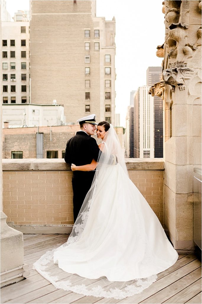 Military wedding portrait of bride in ballgown and cathedral veil with groom in naval uniform overlooking city skyline