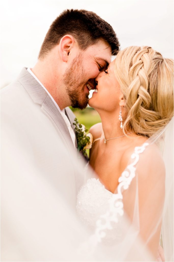 Intimate close-up portrait of a bride and groom about to kiss, with the bride wearing a strapless dress and veil. The image has a bright, airy quality with a light background.