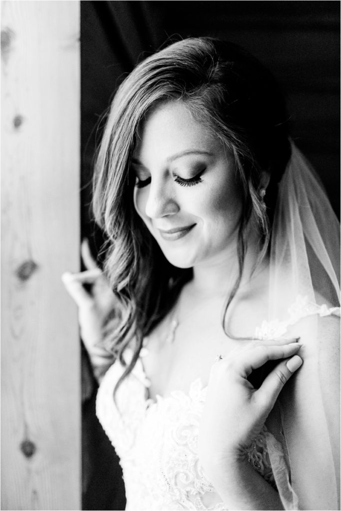 Black and white close-up portrait of a bride looking down with a gentle smile, showing detailed eye makeup and veil, with soft side lighting