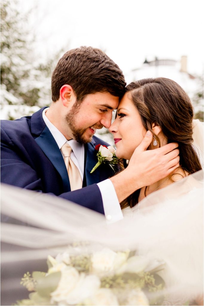 Intimate winter wedding portrait with bride and groom touching foreheads, veil detail in foreground showing natural posing technique