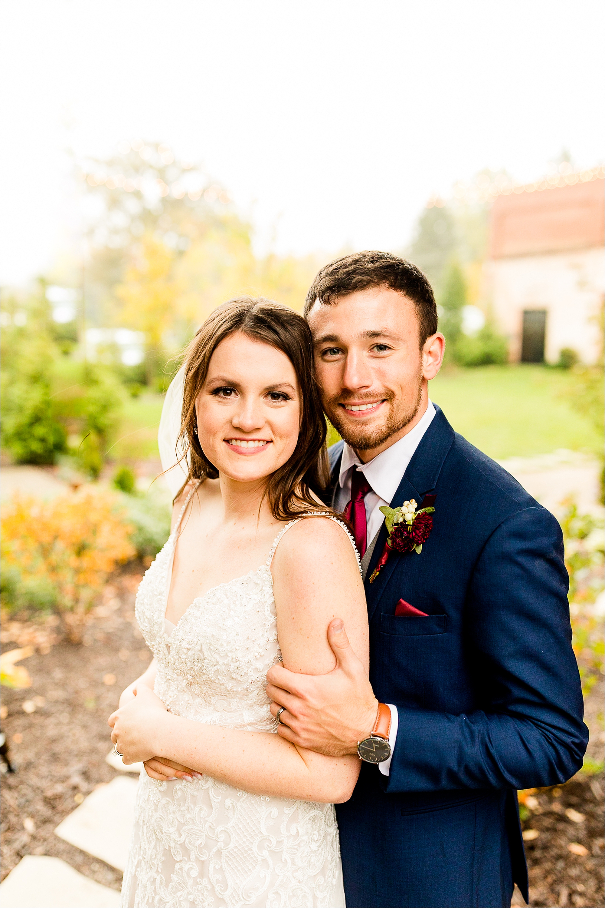 Portrait of bride and groom during golden hour. Bride in beaded spaghetti strap gown and groom in navy suit with burgundy tie and boutonniere, smiling at camera.