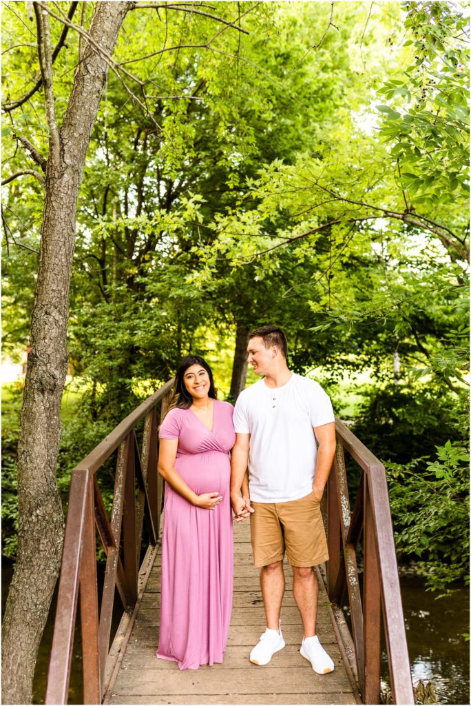 couple stands on bridge during maternity photos in Ewing Park photographed by Bloomington IL maternity photographers Caitlin and Luke Photography