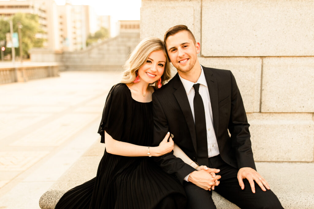 Caitlin and Luke in formal black attire against stone architecture at sunset